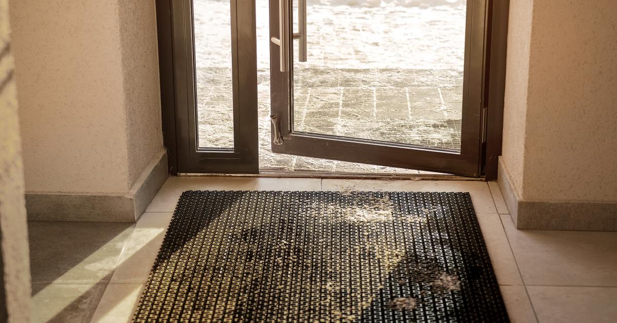 A door threshold that leads to an outdoor environment. There is a black door mat on the ground.