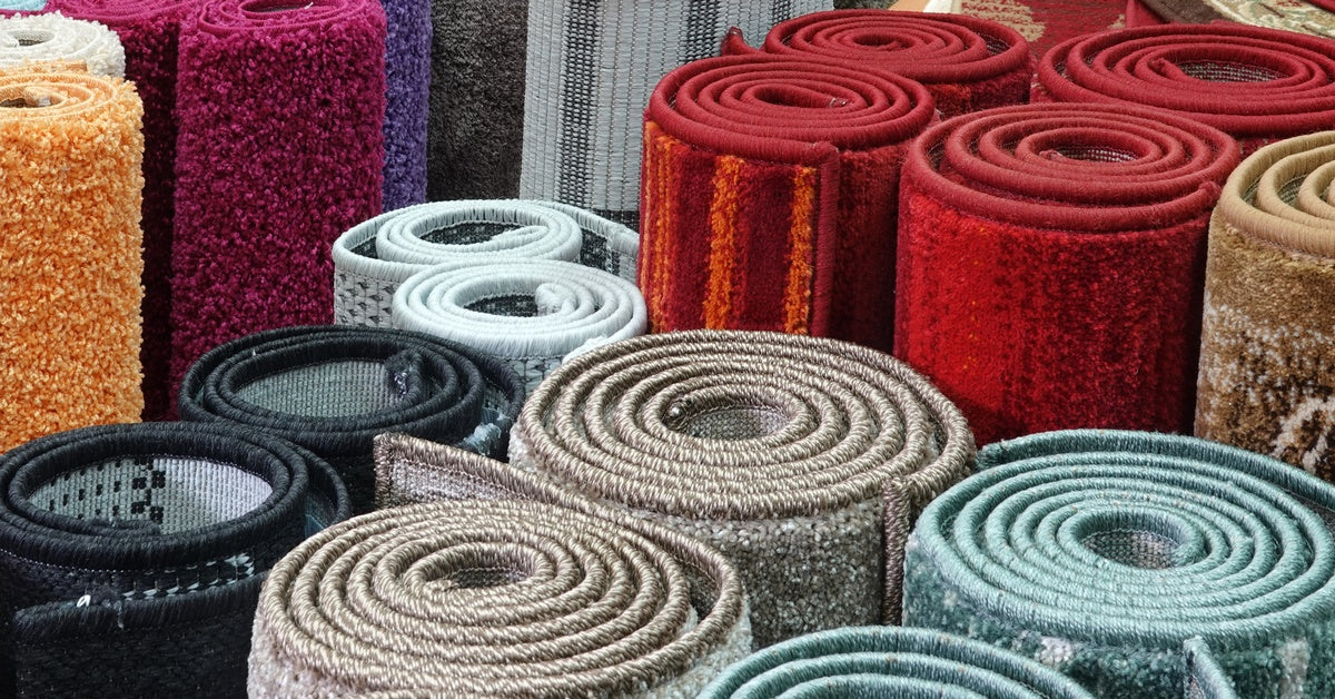 Several rugs are rolled up and placed next to each other. The rugs are all different colors, like red, black, and blue.