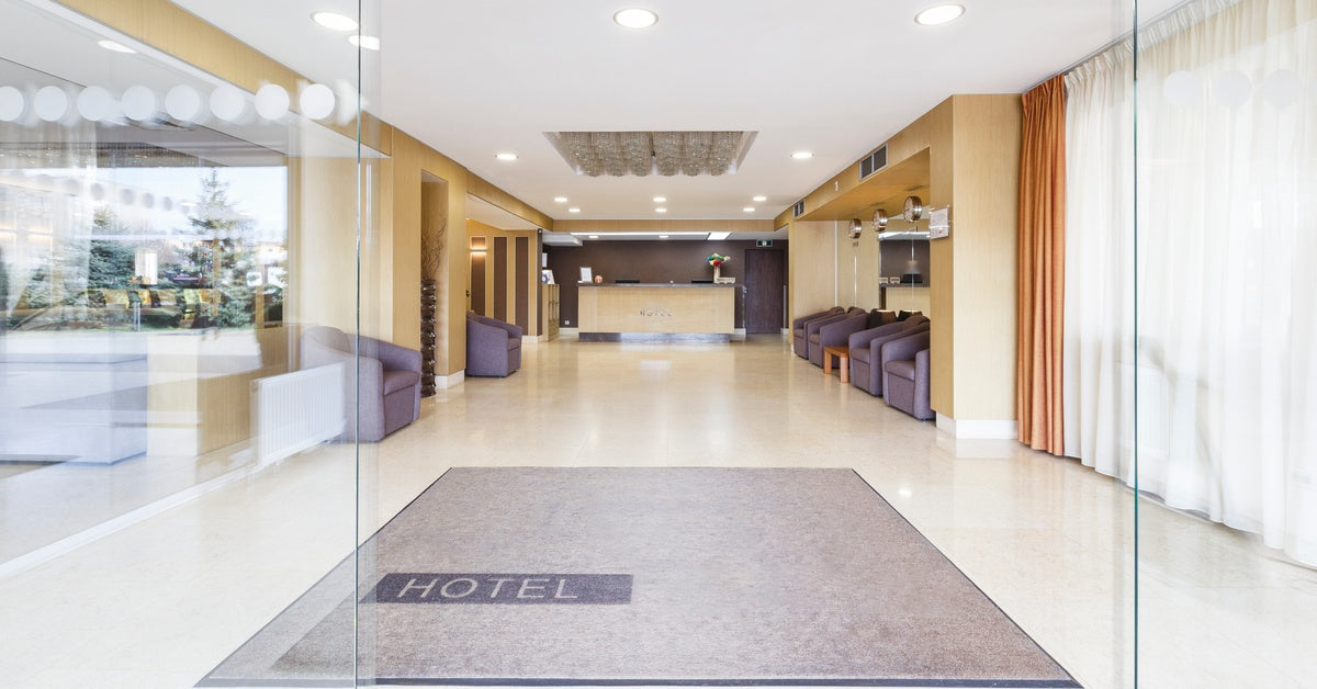 An entrance to a hotel lobby with a welcome mat on the ground and a service desk in the background.