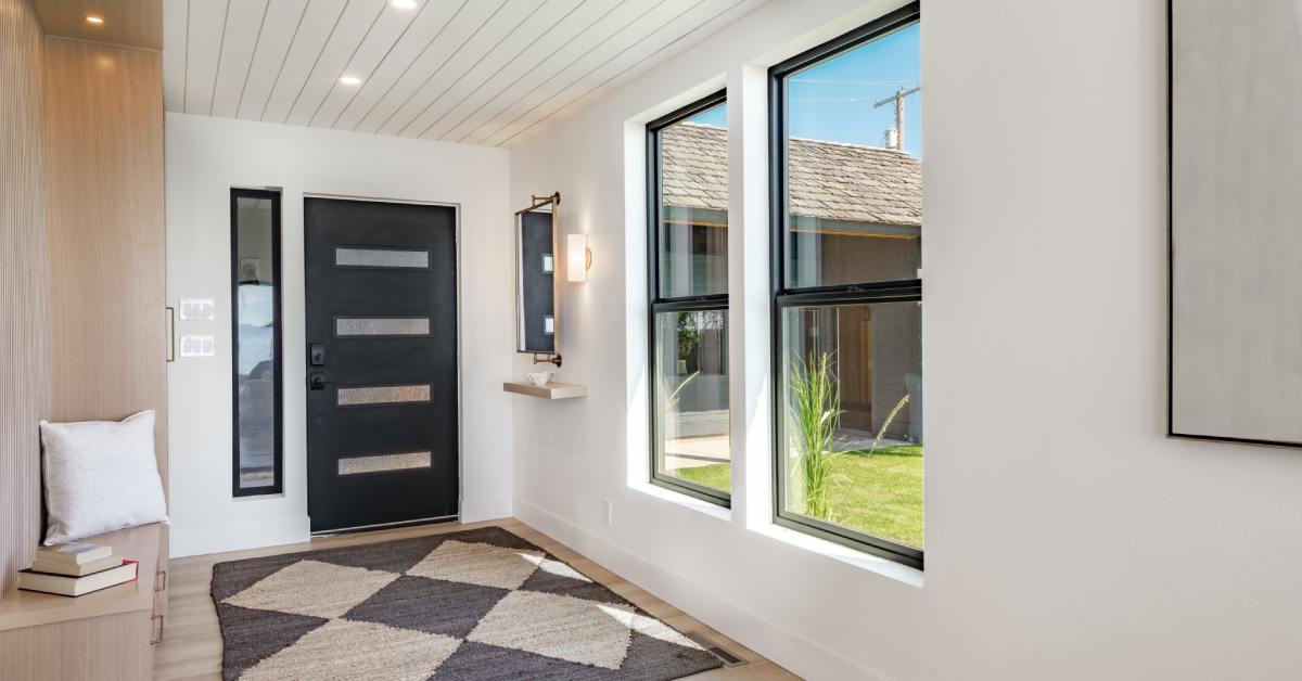 An interior of a residential home. There is a door with a floor mat in front of it and a window looking out to a lawn.