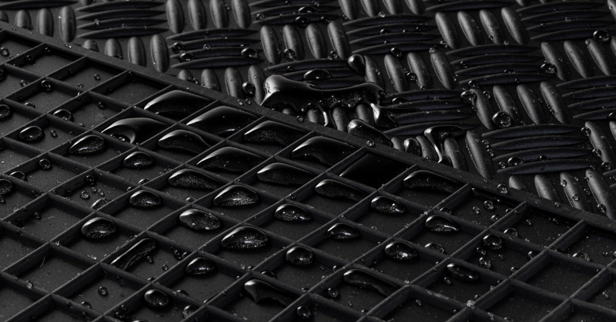 Two black mats, one on top of the other, have little droplets of water on each of them. They’re made out of rubber material.