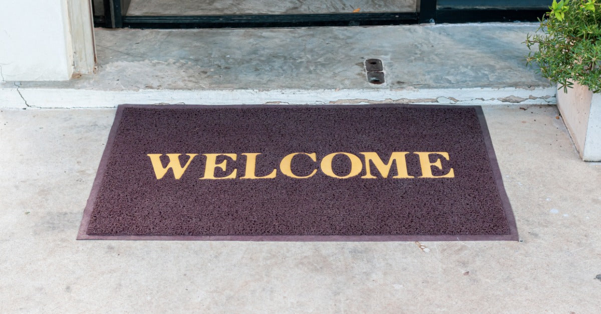 A door mat is placed on the ground in front of a door. The door appears to be a black sliding door.