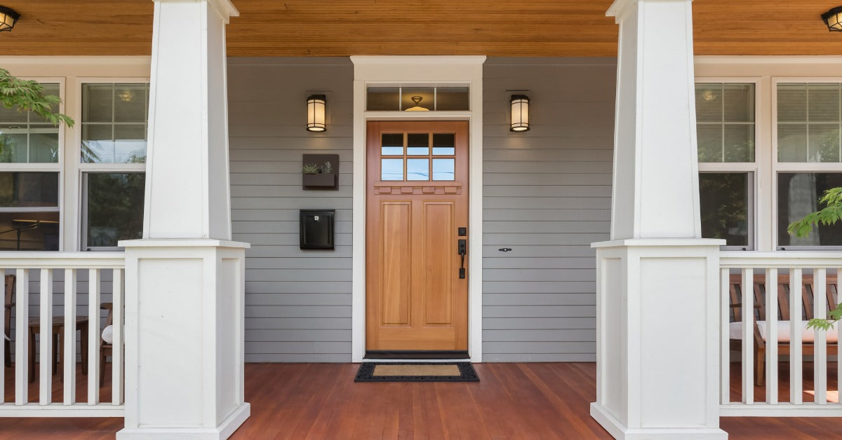 A residential porch with a front door to a home. There is a welcome mat on the ground.