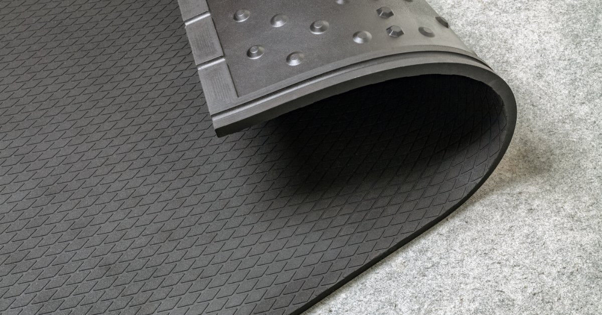 A black, rubber mat is on the ground. It is slightly curled back, revealing bumps on the underside of the mat.