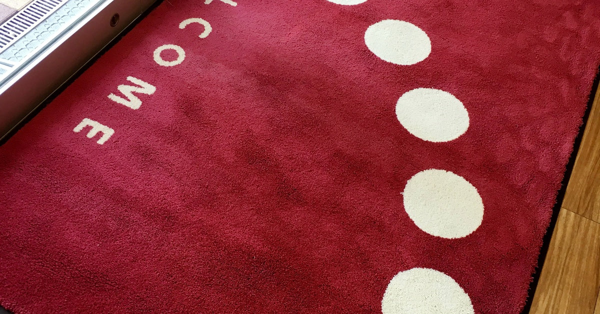 A glass sliding door with a red welcome mat on the ground. The floor under the mat is made of wood.