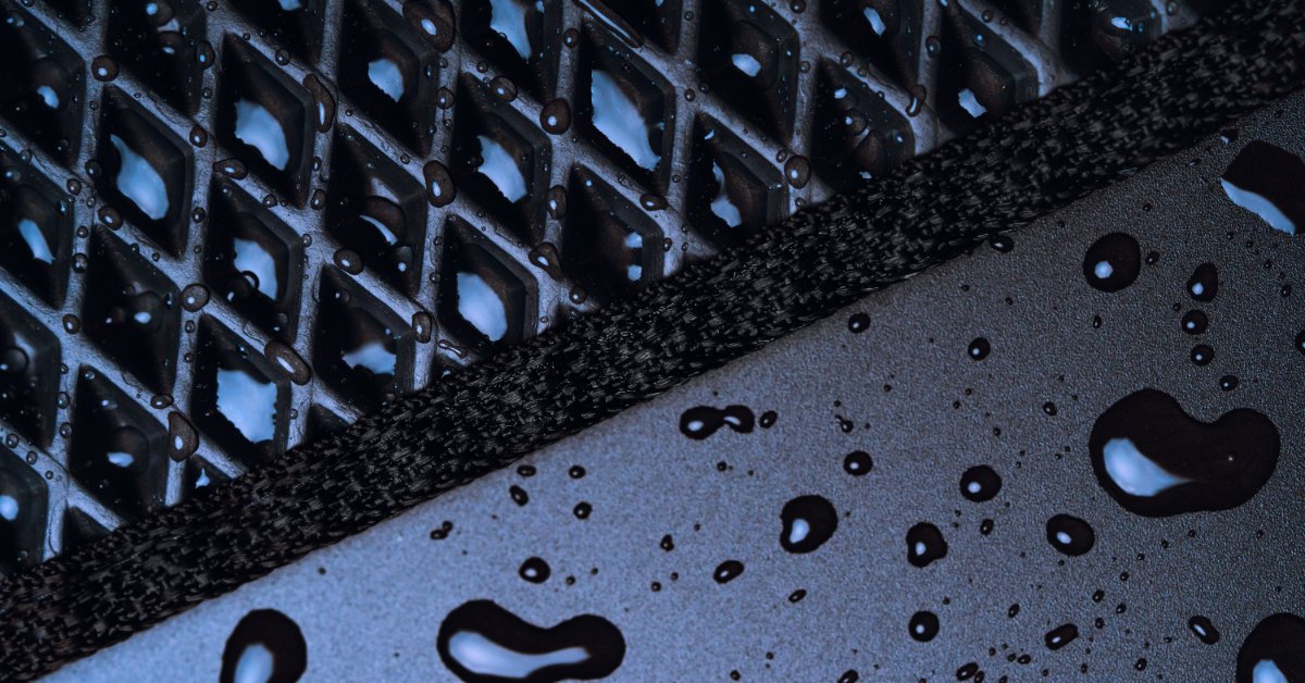 A black mat is on a floor. There are several droplets of water that are on the black floor mat.