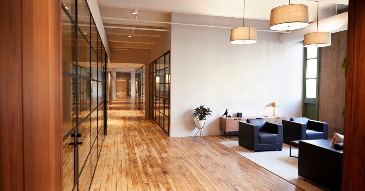 An office space with a hardwood floor and a mat off to the side in a rest area that has chairs and a coffee table.