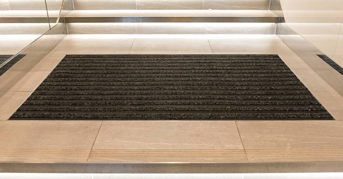 An oversized wiper doormat inside a facility is placed right after the entrance and before the stairs.