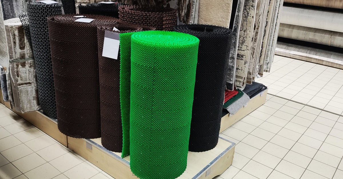 There are several rolls of commercial mats on a display stand. The stand is elevated on a tile floor.