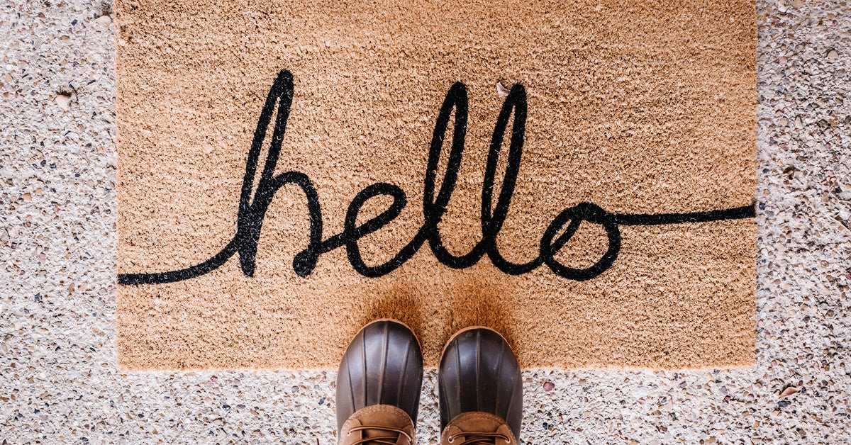 A pair of brown boots on top of a doormat with the word "hello" stitched onto it in black cursive writing.