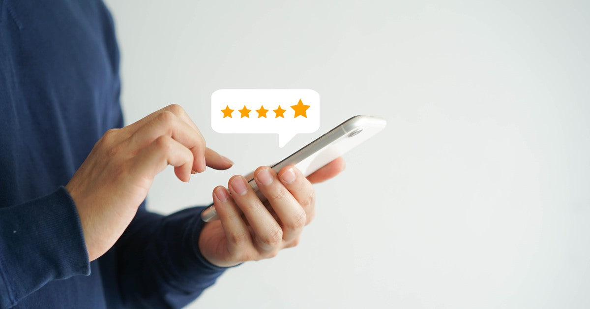 A man holding his white smartphone places a five-star review represented by a floating bubble with five stars.