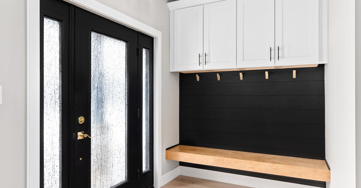 A modern farmhouse mudroom with a black shiplap wall and wood bench. Above the shiplap are white cabinets.